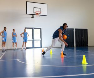 Dribbling basketball around cones, coach training female basketball team in gym, copy space. teamwork, gymnasium, sports, practice, female athletes, exercise